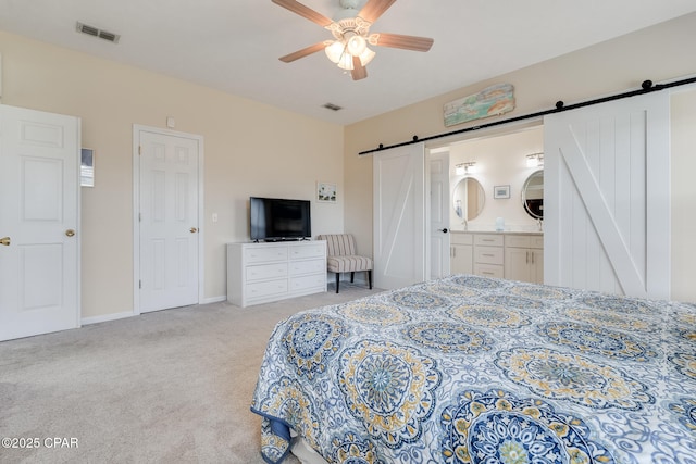 carpeted bedroom with ensuite bath, a barn door, and ceiling fan