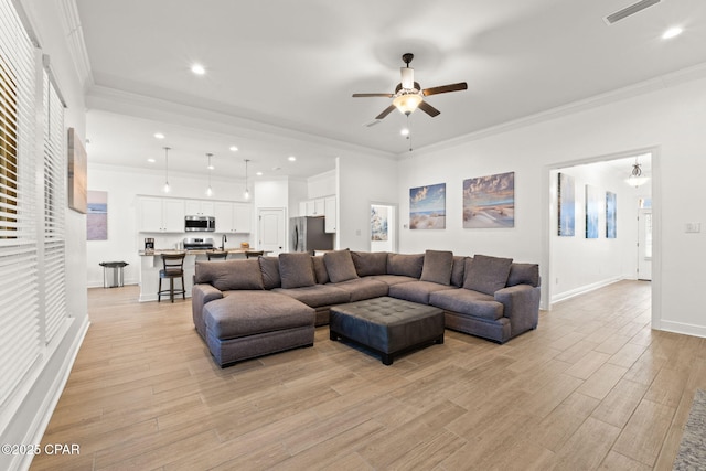 living area with light wood-style flooring, a ceiling fan, baseboards, visible vents, and crown molding