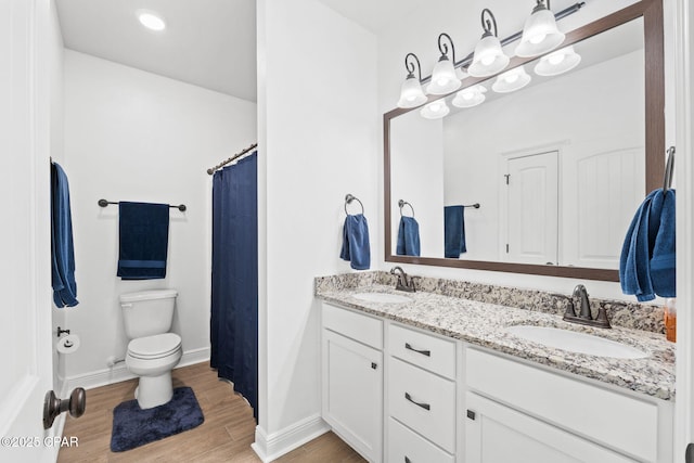 bathroom featuring double vanity, a sink, toilet, and wood finished floors