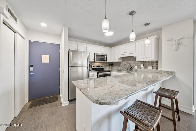 kitchen with sink, white cabinetry, hanging light fixtures, appliances with stainless steel finishes, and kitchen peninsula