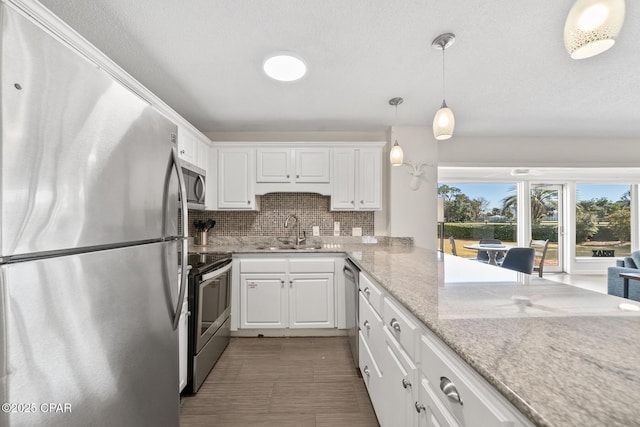 kitchen with sink, white cabinetry, stainless steel appliances, light stone countertops, and decorative light fixtures