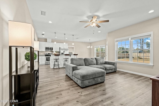 living room with ceiling fan with notable chandelier and light wood-type flooring