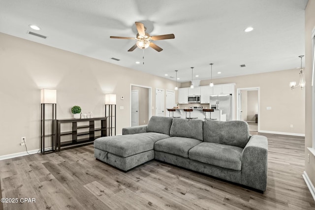 living room with ceiling fan with notable chandelier and light wood-type flooring