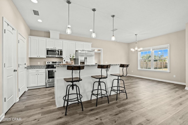 kitchen with white cabinetry, stone countertops, hanging light fixtures, a kitchen island, and stainless steel appliances