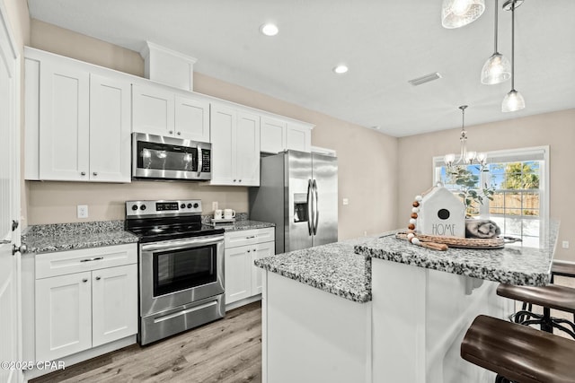 kitchen featuring stainless steel appliances, light stone countertops, hanging light fixtures, and white cabinets