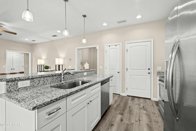 kitchen featuring sink, stainless steel appliances, light stone countertops, white cabinets, and decorative light fixtures