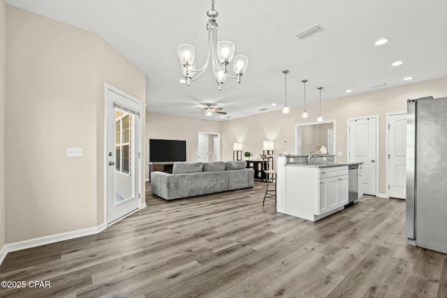 kitchen featuring appliances with stainless steel finishes, a kitchen island with sink, light stone counters, white cabinets, and decorative light fixtures