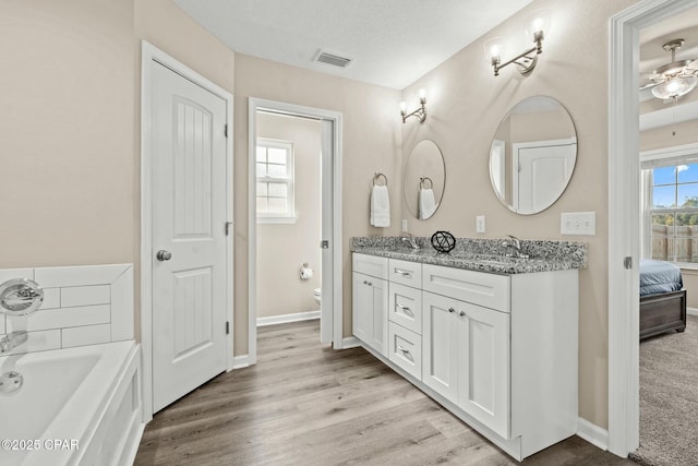 bathroom with a washtub, vanity, wood-type flooring, a textured ceiling, and toilet