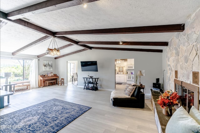 living room with a fireplace, lofted ceiling with beams, a chandelier, light hardwood / wood-style floors, and a textured ceiling