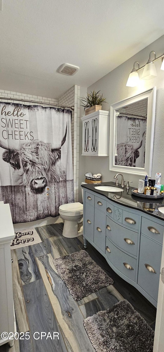 bathroom with toilet, hardwood / wood-style floors, a textured ceiling, walk in shower, and vanity