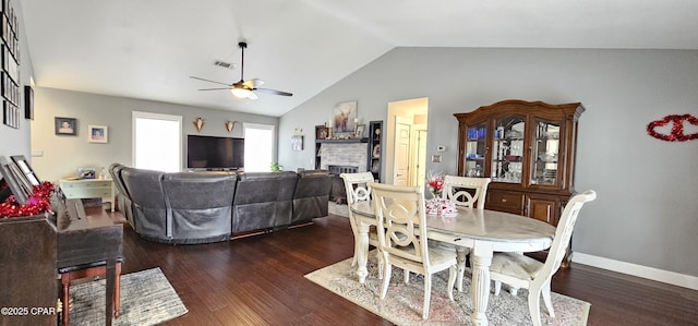 dining area featuring ceiling fan, vaulted ceiling, a brick fireplace, and dark hardwood / wood-style flooring