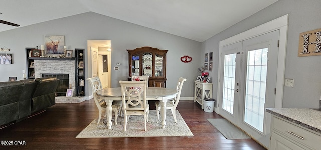 dining room with vaulted ceiling, french doors, dark wood-type flooring, plenty of natural light, and a fireplace