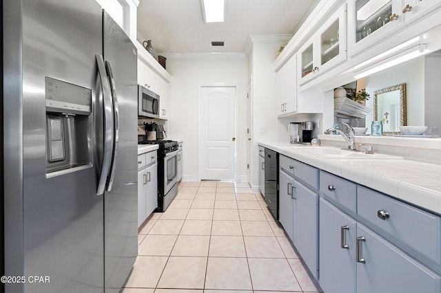 kitchen with appliances with stainless steel finishes, white cabinetry, sink, ornamental molding, and light tile patterned floors