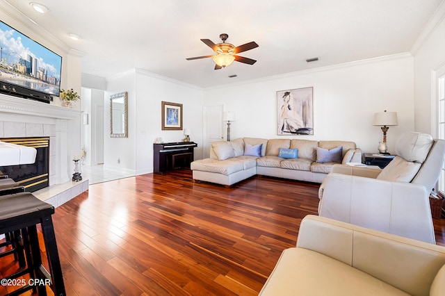 living room with dark hardwood / wood-style flooring, crown molding, a tile fireplace, and ceiling fan