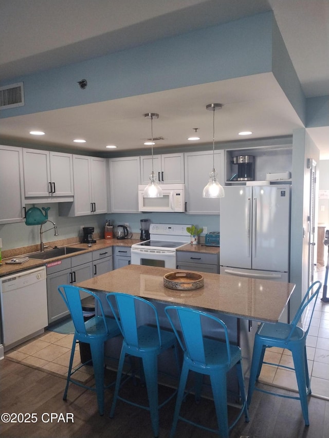 kitchen with white appliances, visible vents, a sink, and a kitchen breakfast bar