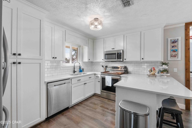 kitchen featuring a breakfast bar, sink, kitchen peninsula, stainless steel appliances, and white cabinets