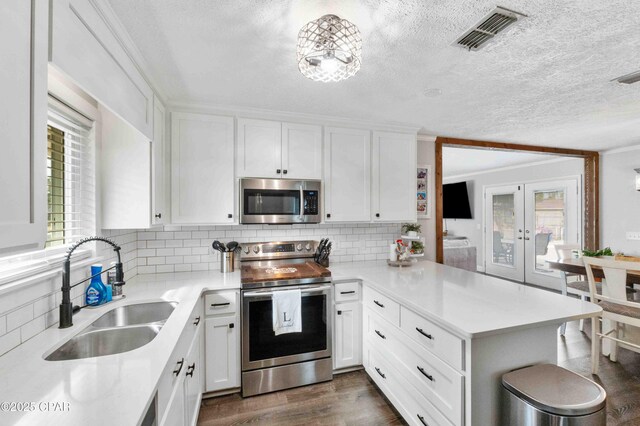 kitchen with sink, appliances with stainless steel finishes, white cabinetry, decorative backsplash, and kitchen peninsula