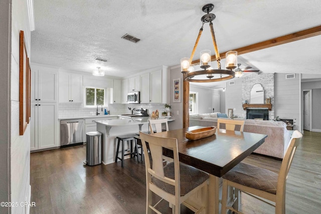 dining room with an inviting chandelier, lofted ceiling with beams, a textured ceiling, dark hardwood / wood-style floors, and a fireplace