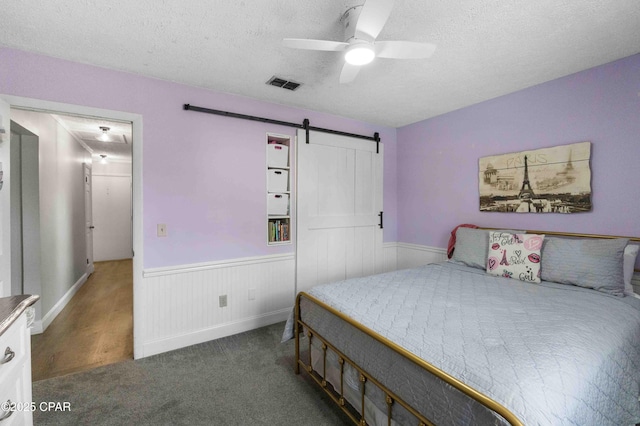 bedroom with a barn door, dark carpet, a textured ceiling, and ceiling fan