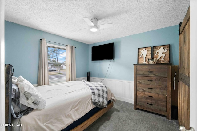 bedroom with ceiling fan, a barn door, carpet, and a textured ceiling