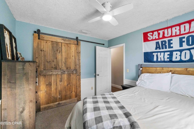 bedroom featuring ceiling fan, a barn door, and a textured ceiling