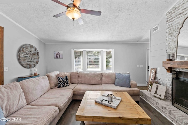 living room featuring crown molding, a textured ceiling, dark hardwood / wood-style floors, ceiling fan, and a fireplace