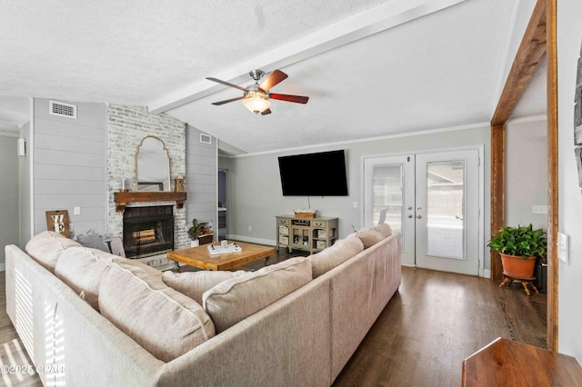 living room featuring french doors, dark wood-type flooring, a textured ceiling, a large fireplace, and ceiling fan