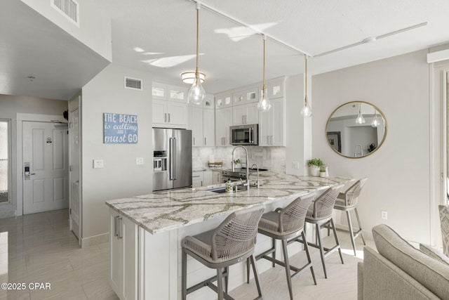 kitchen with a kitchen bar, appliances with stainless steel finishes, white cabinetry, kitchen peninsula, and light stone counters