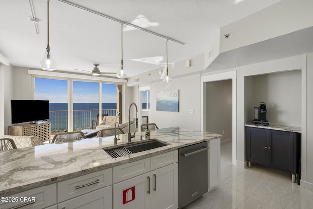 kitchen featuring pendant lighting, a textured ceiling, dishwasher, sink, and light stone counters