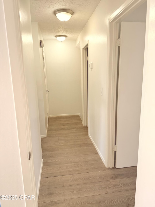 corridor with light hardwood / wood-style floors and a textured ceiling