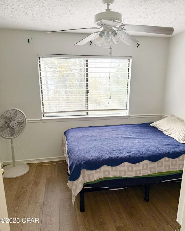 bedroom featuring ceiling fan, multiple windows, wood-type flooring, and a textured ceiling