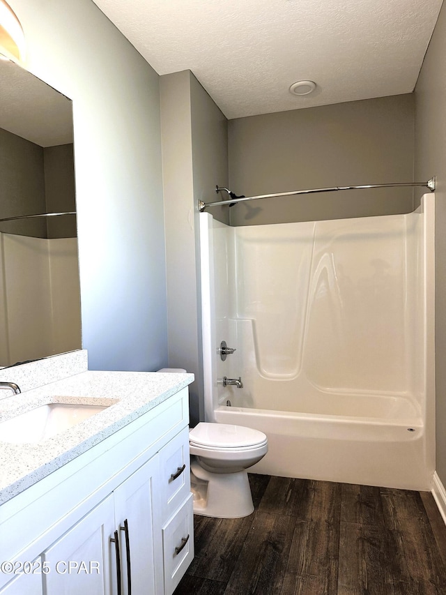 full bathroom with hardwood / wood-style flooring, vanity, shower / bath combination, toilet, and a textured ceiling