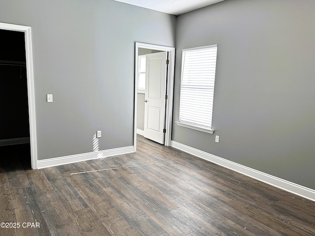 unfurnished bedroom featuring dark hardwood / wood-style flooring, multiple windows, and a spacious closet