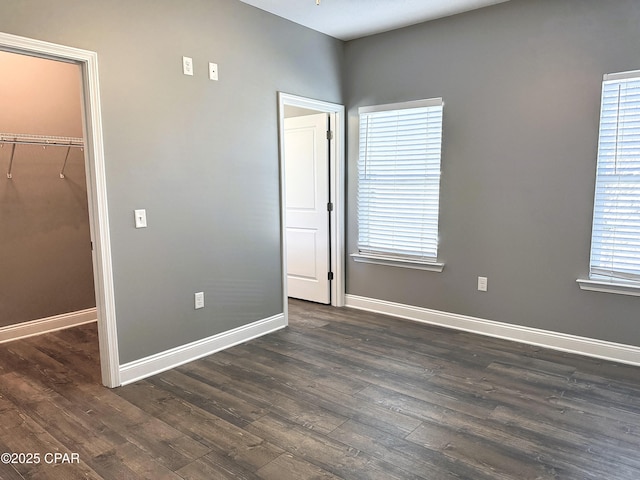 unfurnished bedroom featuring dark hardwood / wood-style flooring, multiple windows, and a walk in closet