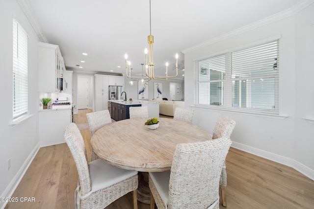 dining area featuring an inviting chandelier, ornamental molding, sink, and light hardwood / wood-style floors