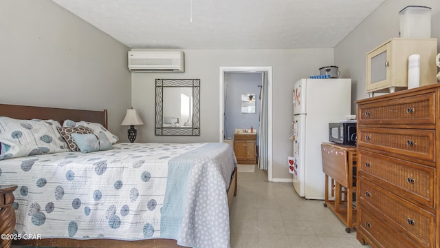 bedroom with an AC wall unit, a textured ceiling, white refrigerator, and ensuite bath