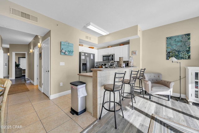 kitchen with white cabinets, appliances with stainless steel finishes, a kitchen breakfast bar, kitchen peninsula, and light tile patterned floors