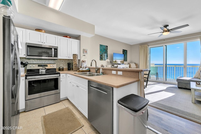 kitchen with white cabinets, stainless steel appliances, sink, kitchen peninsula, and light tile patterned floors