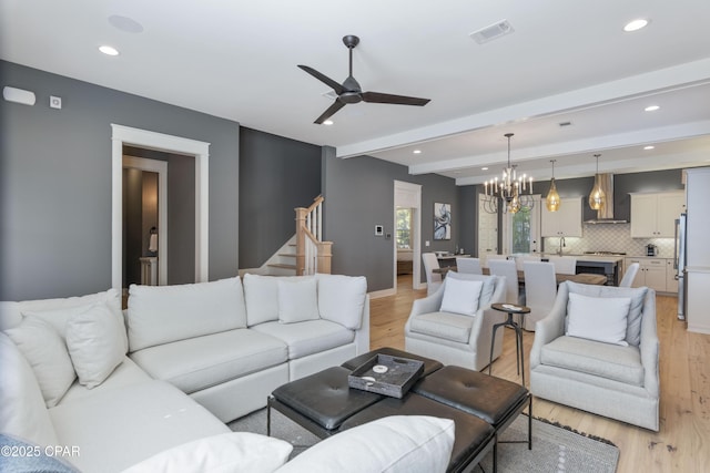 living room with ceiling fan with notable chandelier, beamed ceiling, and light wood-type flooring