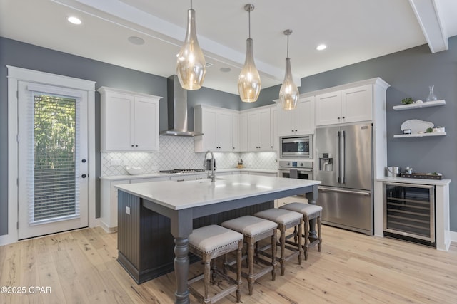 kitchen with white cabinets, appliances with stainless steel finishes, beverage cooler, and wall chimney range hood