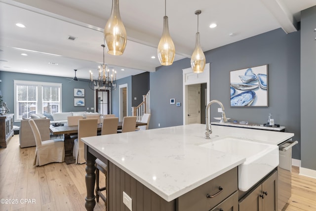 kitchen with light stone counters, decorative light fixtures, light wood-type flooring, an island with sink, and beam ceiling