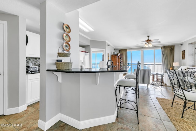 kitchen featuring white cabinetry, white refrigerator with ice dispenser, a breakfast bar area, and crown molding