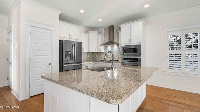 kitchen with appliances with stainless steel finishes, white cabinets, a kitchen island with sink, light stone counters, and wall chimney exhaust hood