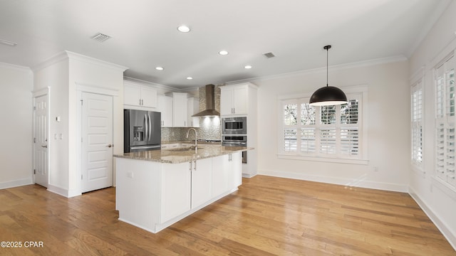 kitchen featuring sink, white cabinetry, an island with sink, stainless steel appliances, and wall chimney range hood