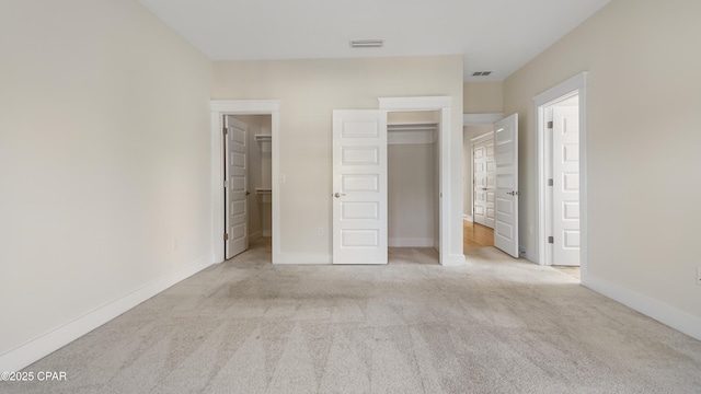 unfurnished bedroom featuring ensuite bathroom, a spacious closet, light colored carpet, and a closet