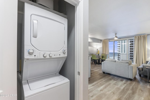 laundry area with laundry area, stacked washer / dryer, light wood finished floors, and ceiling fan