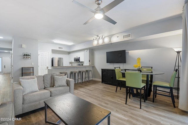 living room featuring visible vents, light wood-style flooring, baseboards, and a ceiling fan