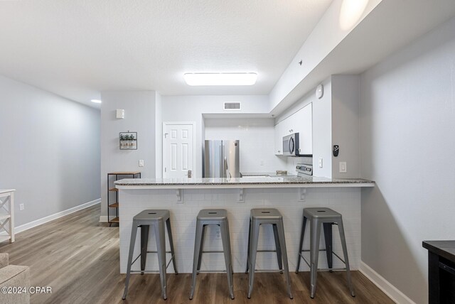 kitchen featuring a kitchen bar, white cabinetry, kitchen peninsula, stainless steel appliances, and hardwood / wood-style floors