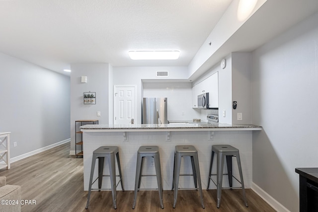 kitchen featuring visible vents, appliances with stainless steel finishes, a peninsula, wood finished floors, and white cabinets