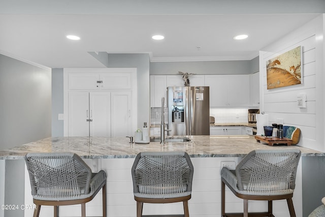 kitchen featuring white cabinets, crown molding, light stone countertops, and stainless steel refrigerator with ice dispenser